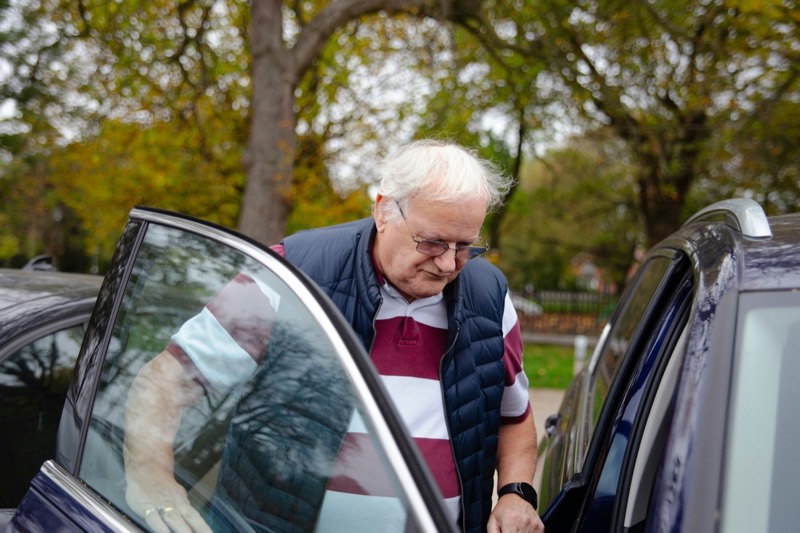 Älterer Herr steigt vorsichtig in ein dunkles Auto